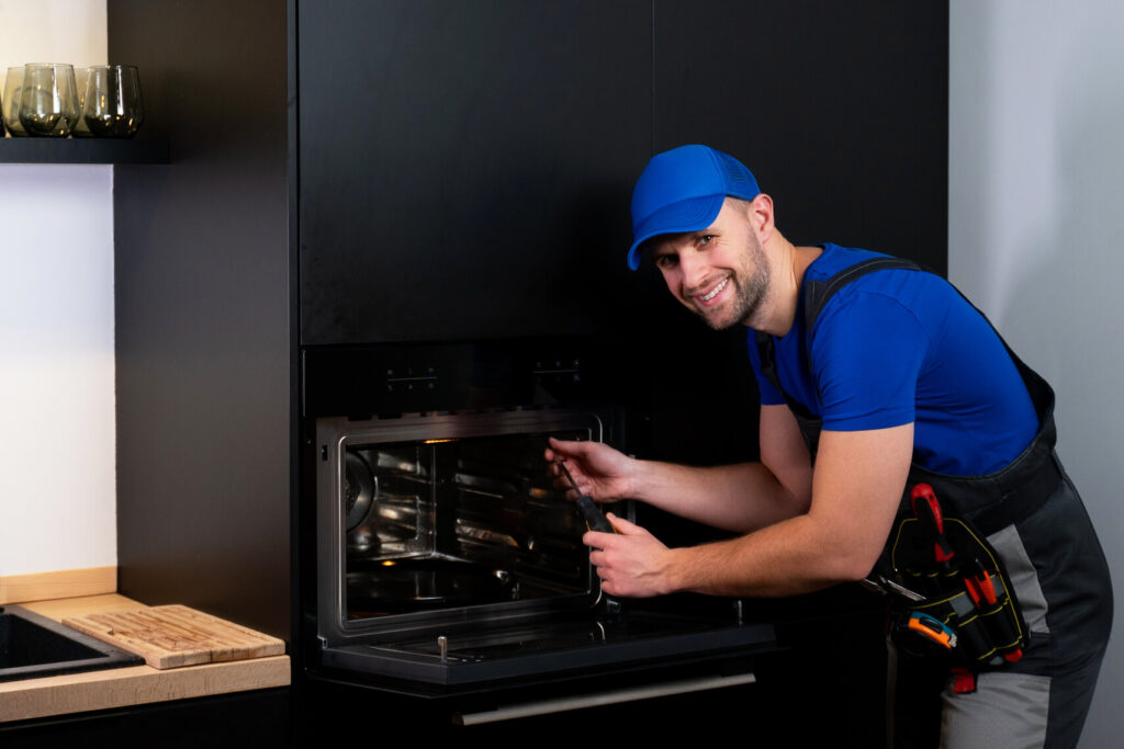 repairman worker uniform inspects oven with screwdriver kitchen concept rep
